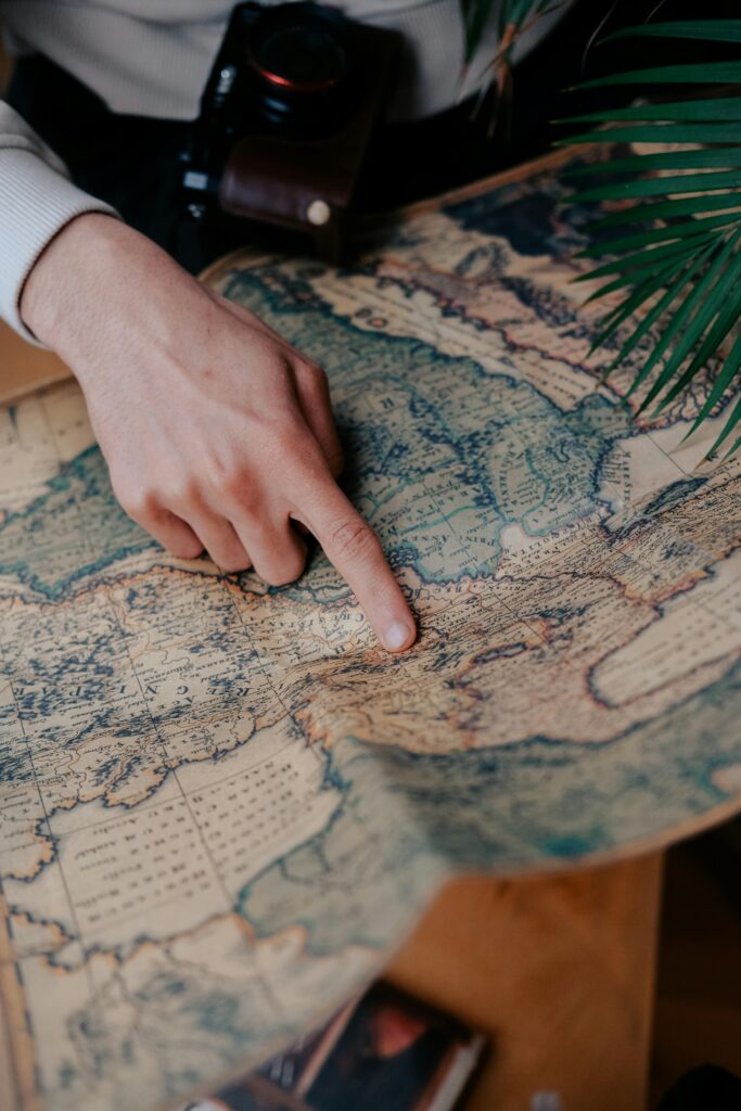 Close-up of a hand pointing to a location on a vintage world map, surrounded by lush greenery.