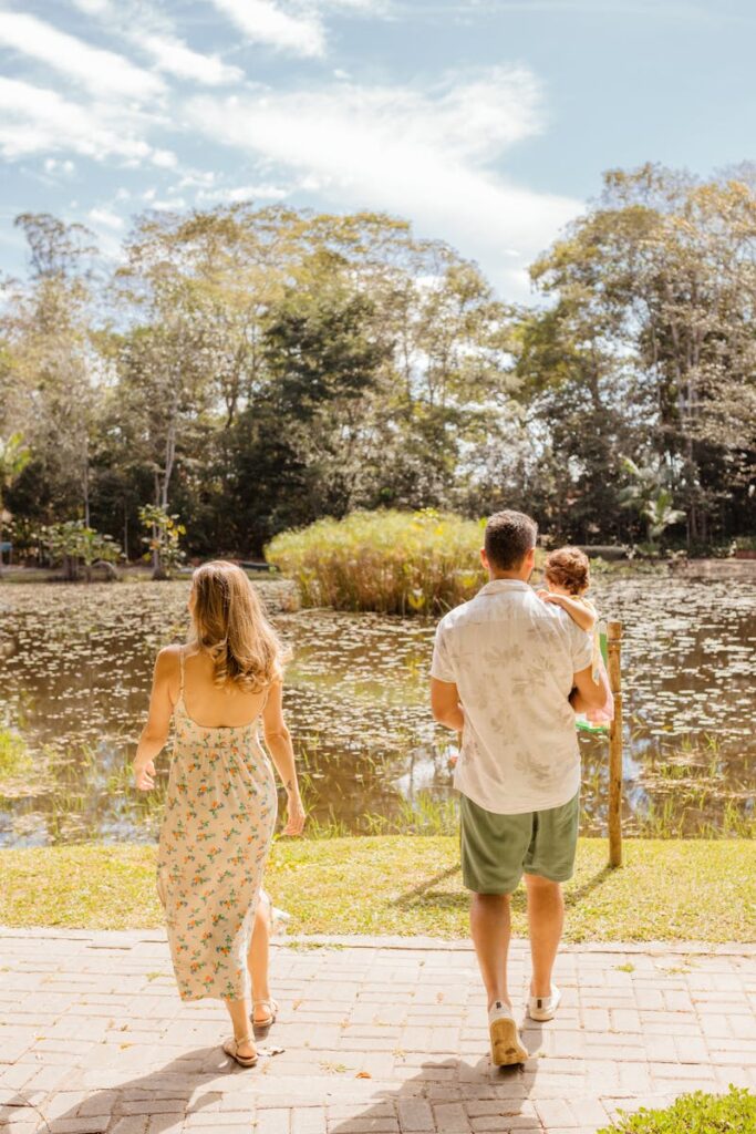 Family enjoying a summer day walk by a pond surrounded by greenery.