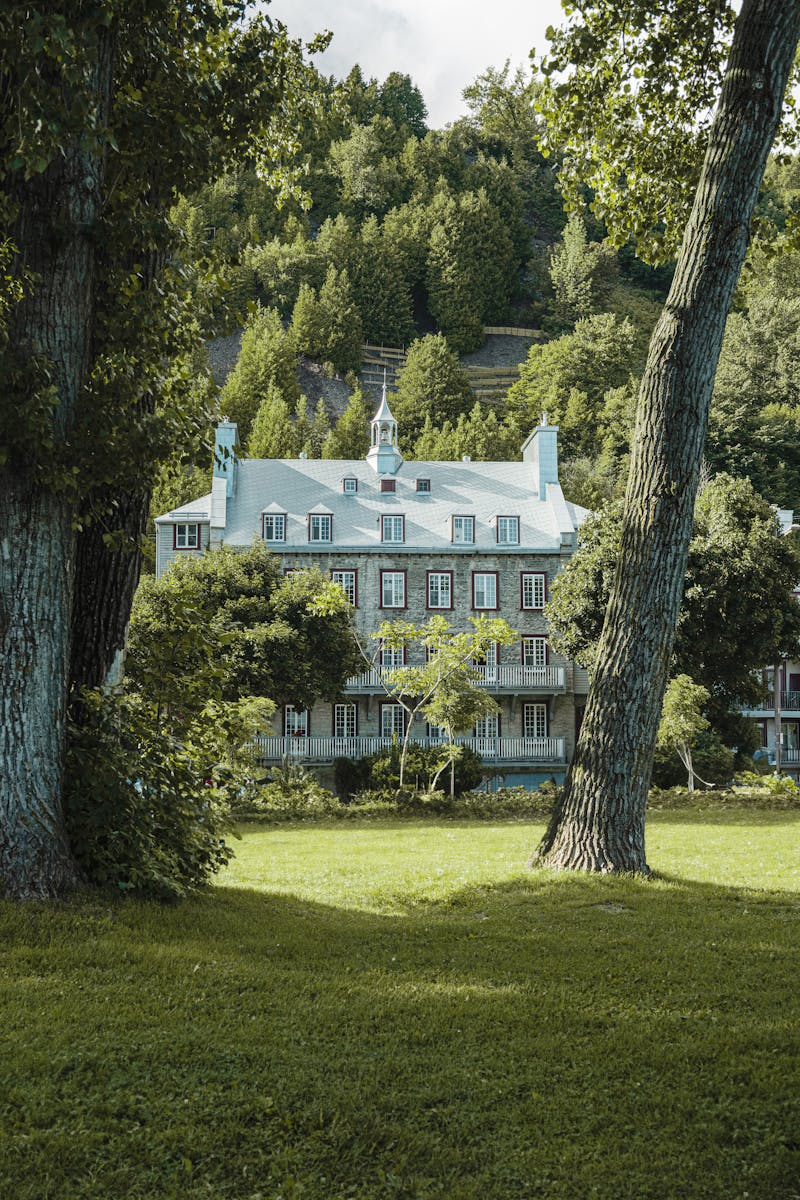 Charming mansion surrounded by lush trees in a Québec park, captured in summer.