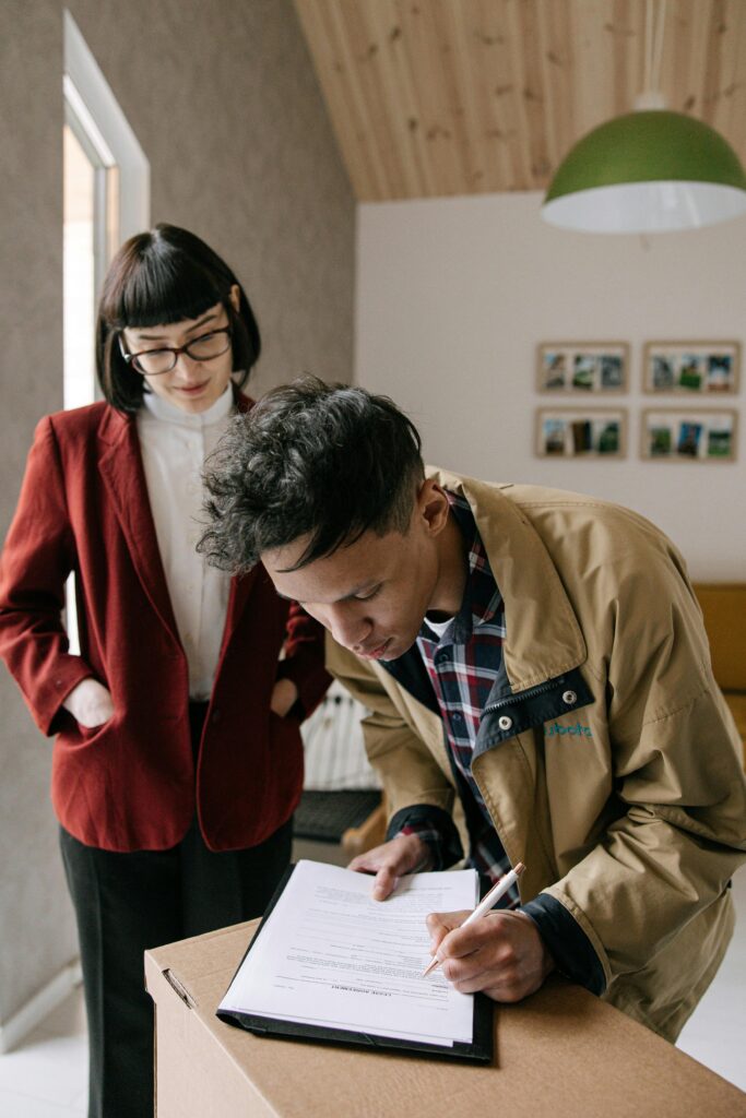 A young man signs a document while a woman observes, set in a modern office environment.