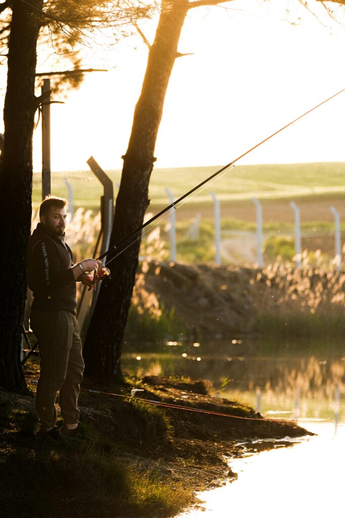 Silhouette of a fisherman angling by a serene pond during sunset, capturing tranquility.