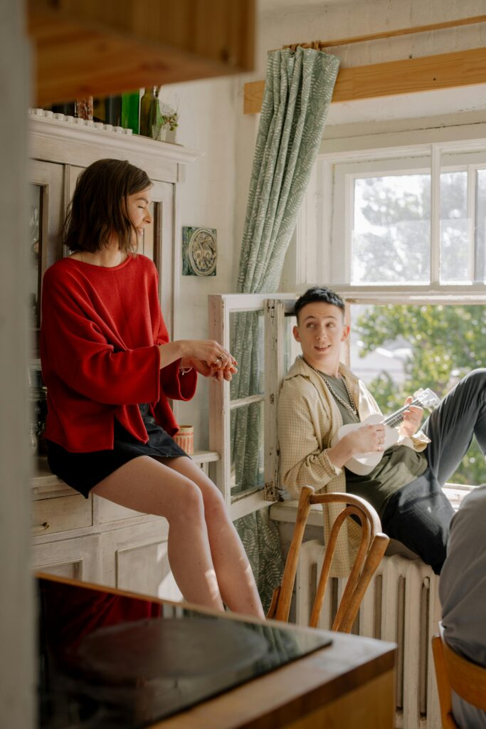 Two young adults enjoying leisure time indoors by a window with a ukulele.